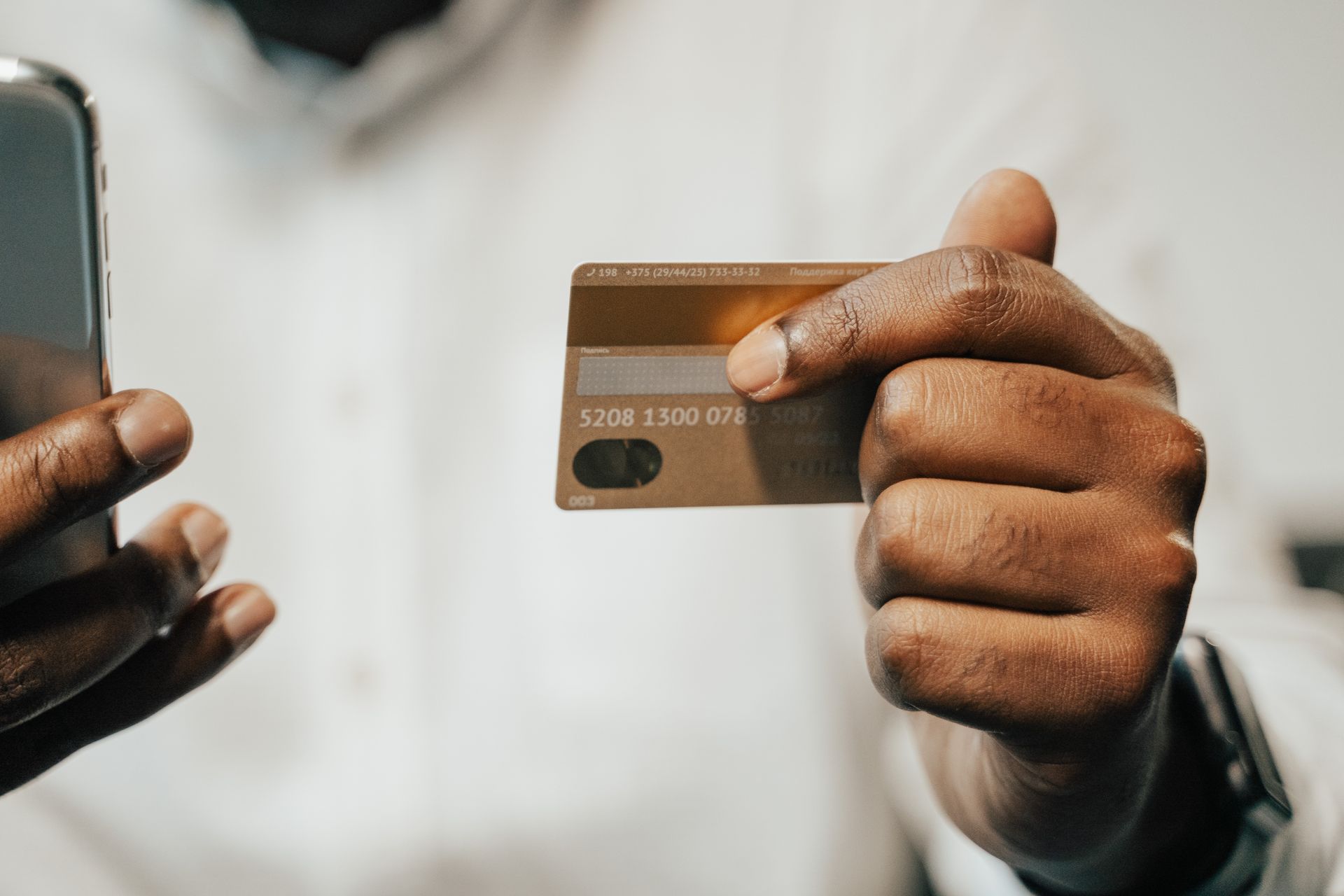 La main d'une personne tenant une carte bancaire à côté d'un téléphone intelligent