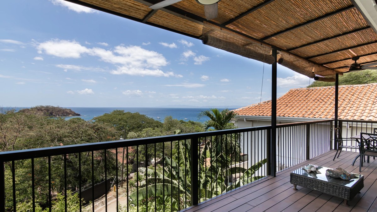 A covered balcony with a black railing and a view over green hillsides and the ocean in Playa Ocotal, Guanacaste