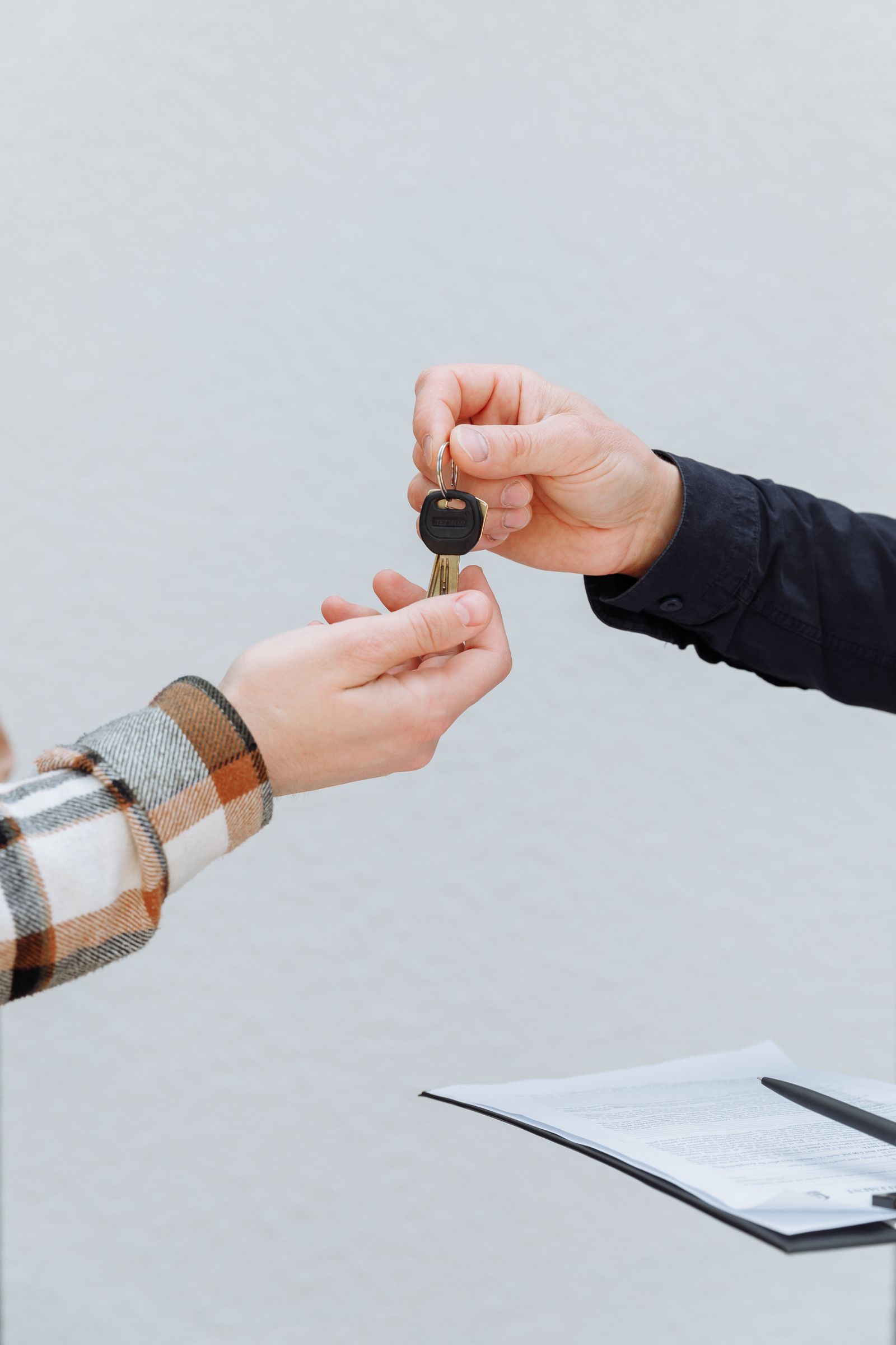 A person handing over house keys to another person, with a signed contract on the table below