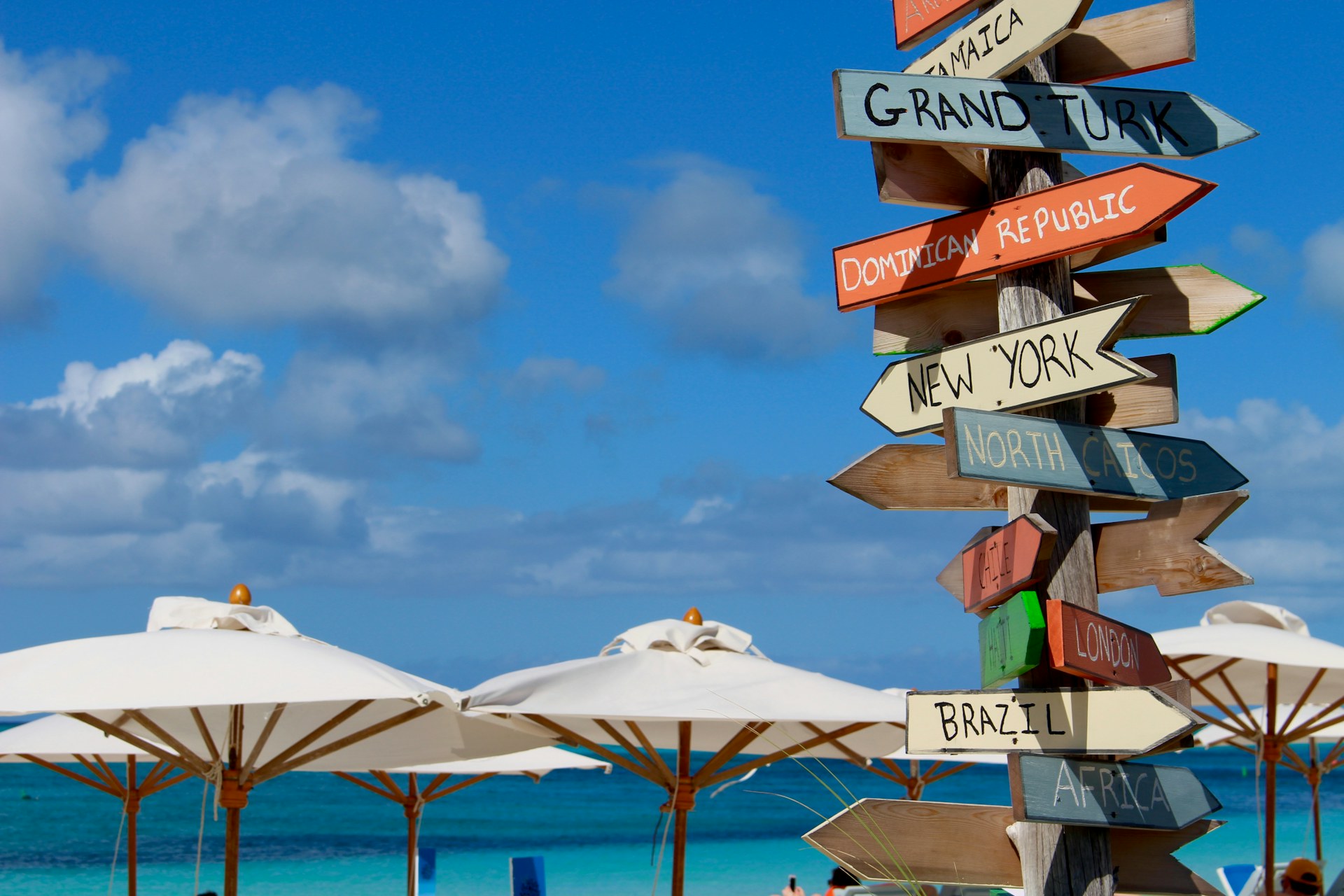 A wooden signpost with arrows pointing toward different beach destinations, planted in the sand