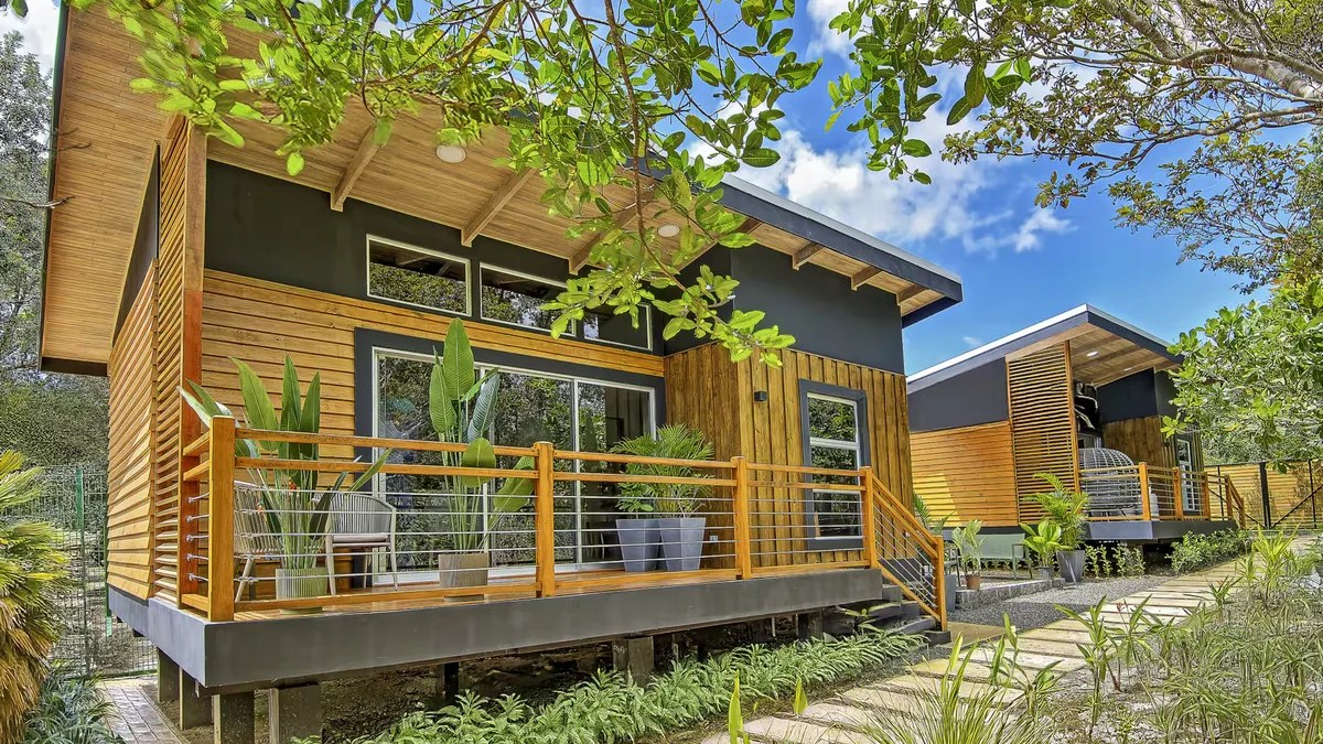 Une maison Harmony à Curubandé, au Guanacaste, avec un revêtement en bois, une terrasse surélevée et des arbres tropicaux