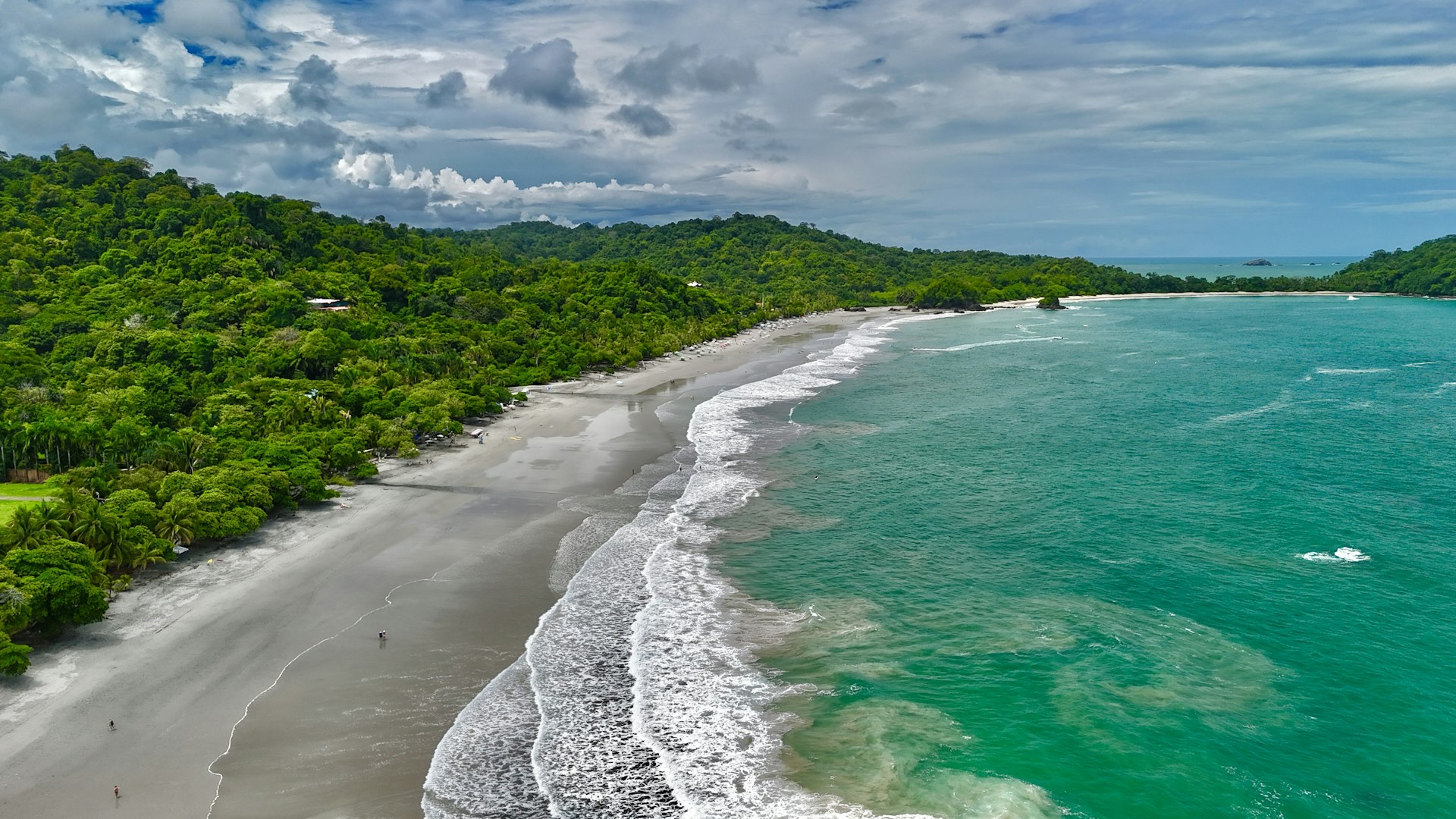 Aerial view of a long Pacific beach in Costa Rica, with the tree line set back from the sand
