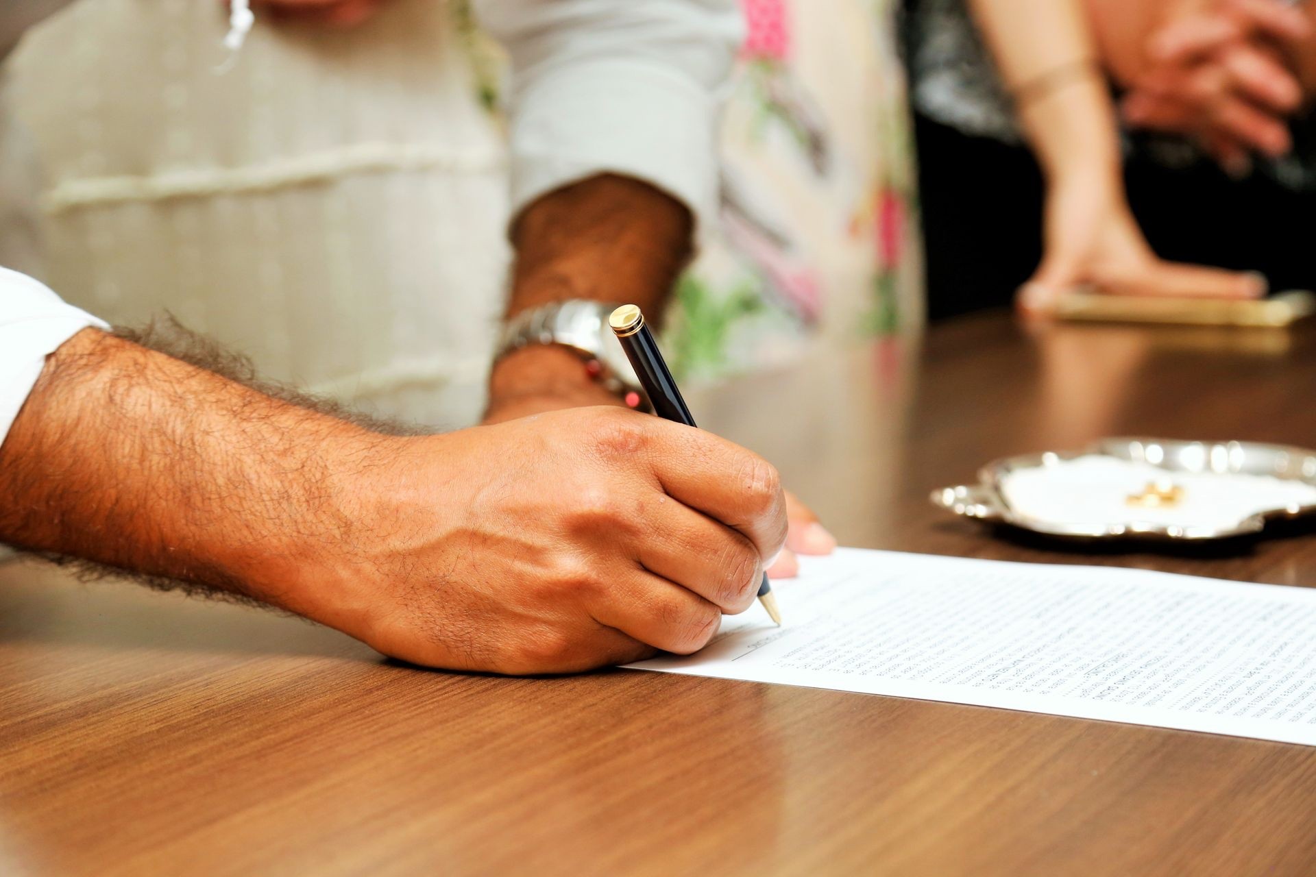 A hand signing a legal document with a pen at a wooden desk