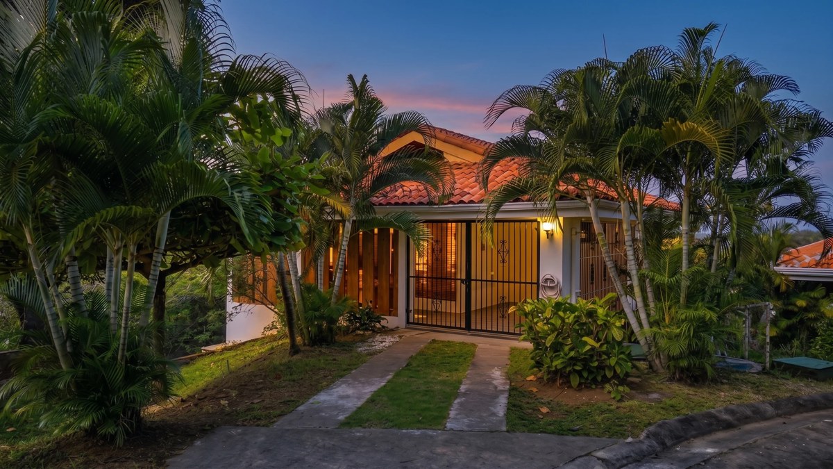 A Costa Rican home glowing at dusk among palm trees, photographed for a real estate listing