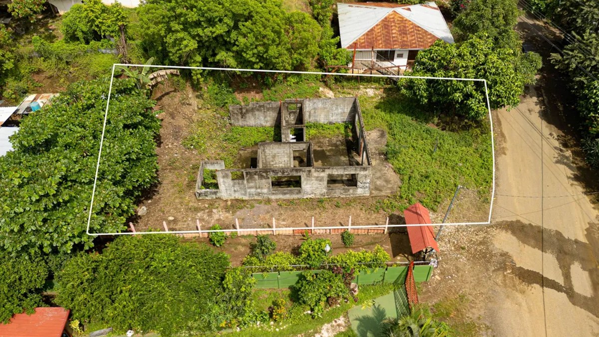 Aerial view of a small lot in Playas del Coco with its boundary outlined in white, beside a dirt road and neighboring homes