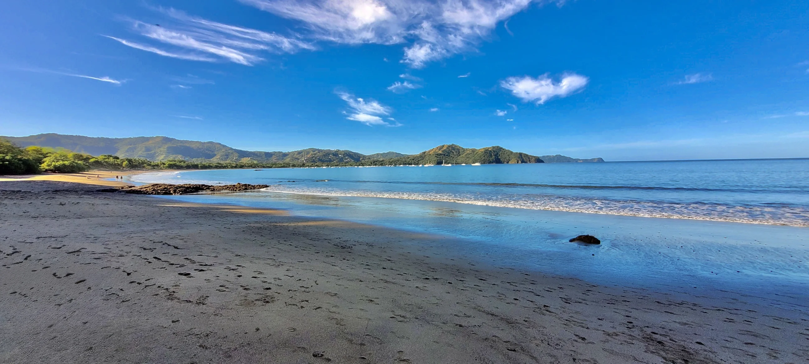 Pale sand beach with footprints leading to calm turquoise water in a quiet Guanacaste bay, Costa Rica